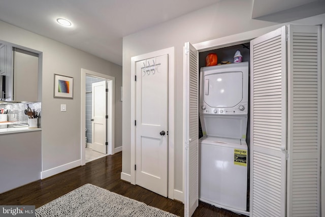 washroom with dark wood-type flooring, laundry area, baseboards, and stacked washing maching and dryer