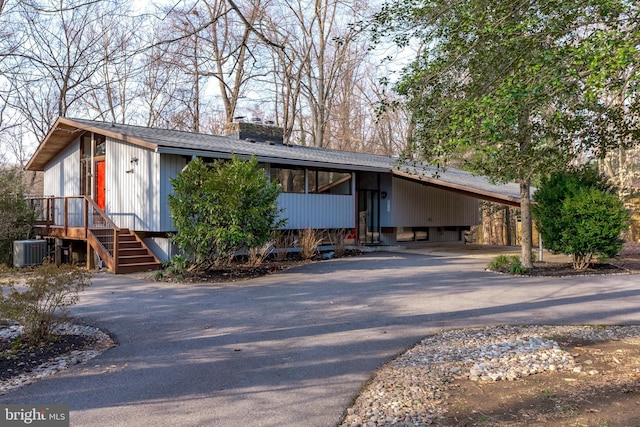 view of front facade with aphalt driveway, central AC unit, a chimney, and a carport