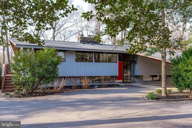 mid-century home featuring driveway and a chimney