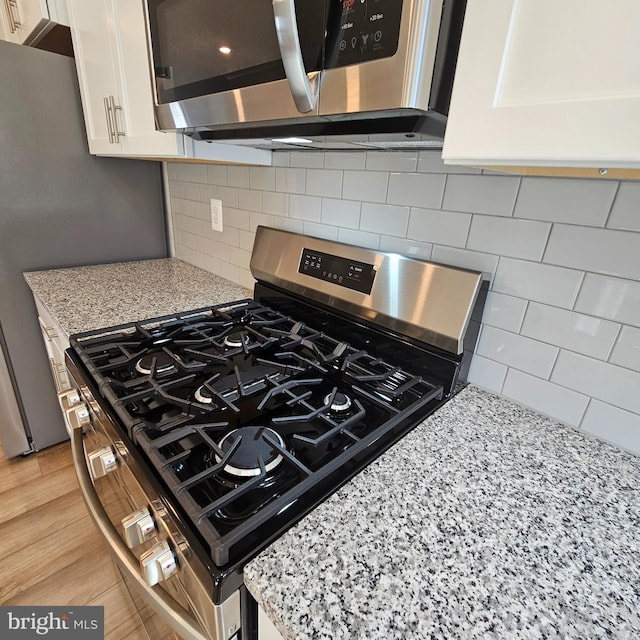 kitchen with light wood-style flooring, backsplash, appliances with stainless steel finishes, white cabinetry, and light stone countertops