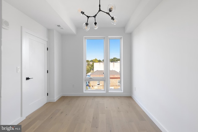 unfurnished dining area with light wood finished floors, baseboards, visible vents, and an inviting chandelier