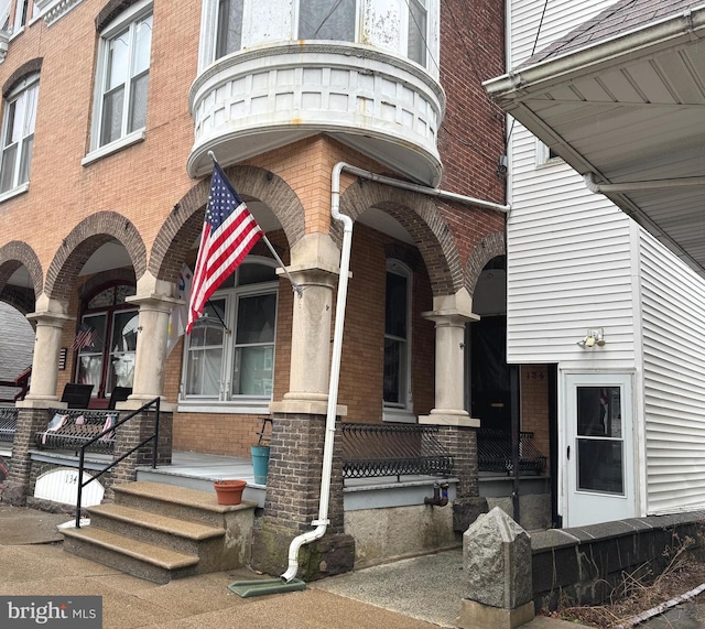 doorway to property with covered porch and brick siding