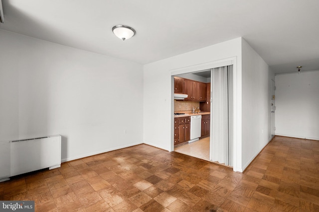 interior space featuring under cabinet range hood, light countertops, dishwasher, tasteful backsplash, and radiator heating unit