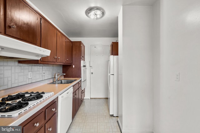 kitchen with light floors, light countertops, a sink, white appliances, and under cabinet range hood