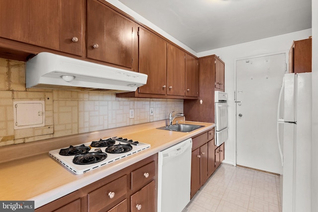 kitchen with under cabinet range hood, white appliances, a sink, light countertops, and light floors