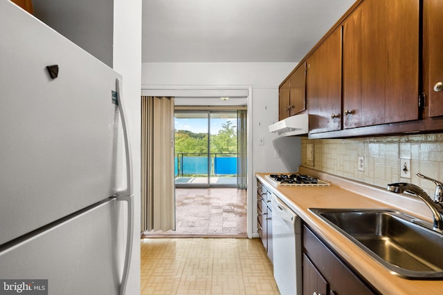 kitchen with white appliances, decorative backsplash, light countertops, under cabinet range hood, and a sink