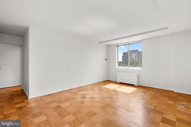 empty room with baseboards, a city view, and radiator