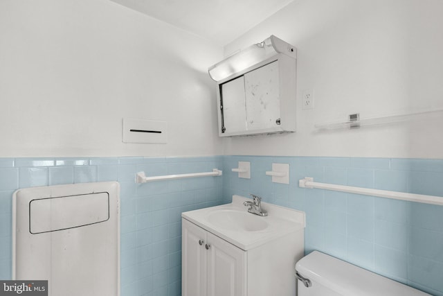 half bathroom with tile walls, a wainscoted wall, vanity, and toilet