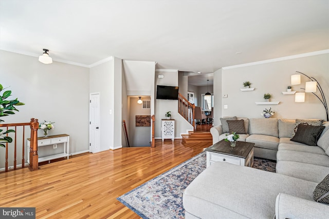 living area featuring stairs, wood finished floors, baseboards, and ornamental molding