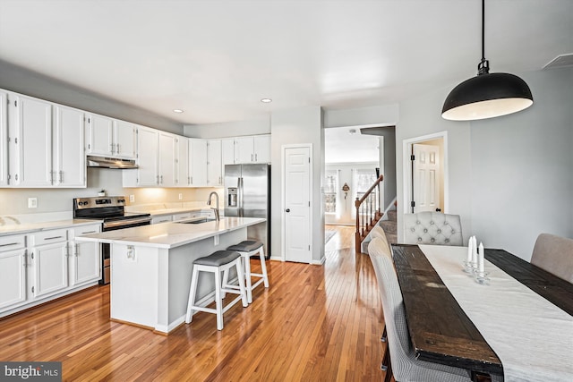 kitchen featuring under cabinet range hood, a sink, stainless steel appliances, white cabinets, and light wood finished floors