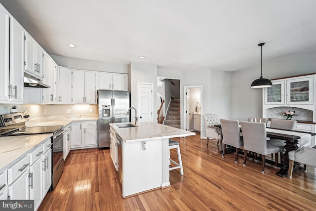 kitchen with under cabinet range hood, white cabinets, stainless steel appliances, wood-type flooring, and a sink