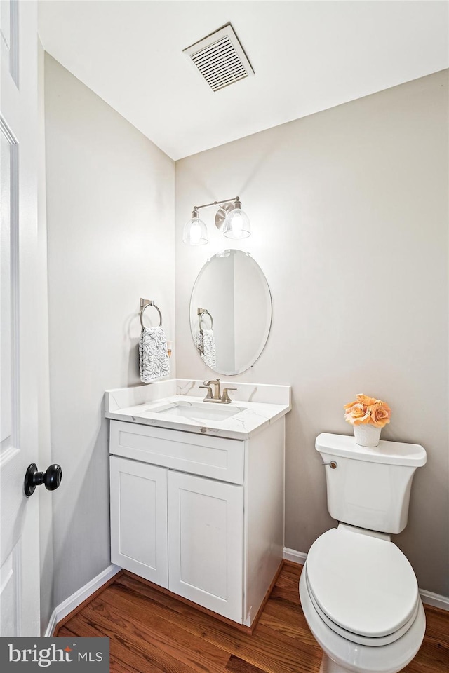 half bath featuring vanity, wood finished floors, visible vents, and baseboards