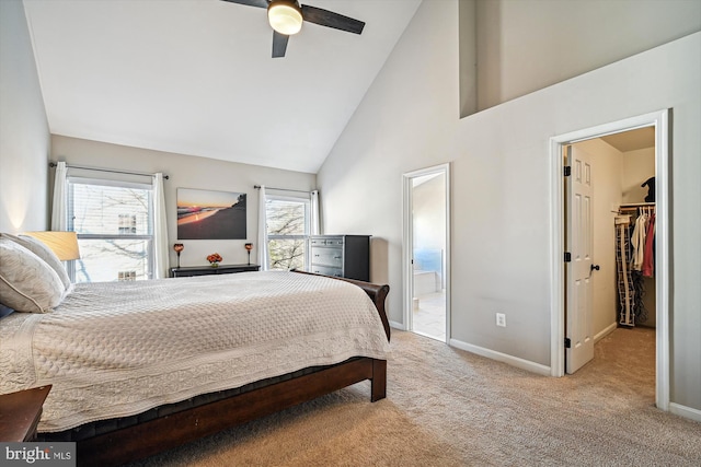 carpeted bedroom featuring a walk in closet, high vaulted ceiling, ensuite bath, baseboards, and ceiling fan