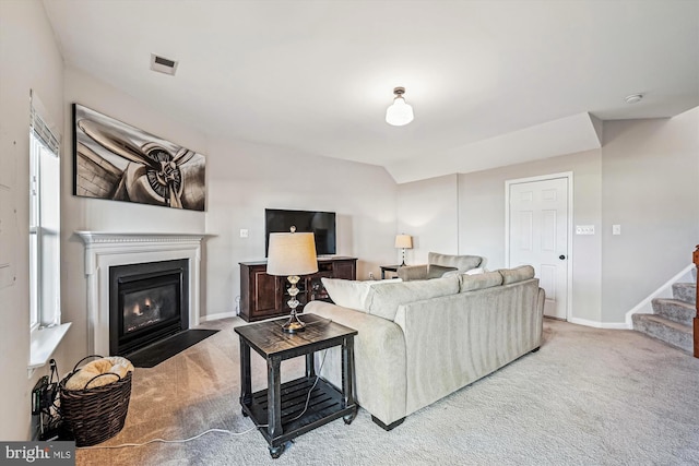 living area with carpet, baseboards, lofted ceiling, a fireplace with flush hearth, and stairs