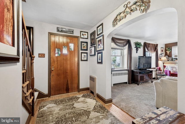 foyer with baseboards, arched walkways, wood finished floors, and radiator heating unit