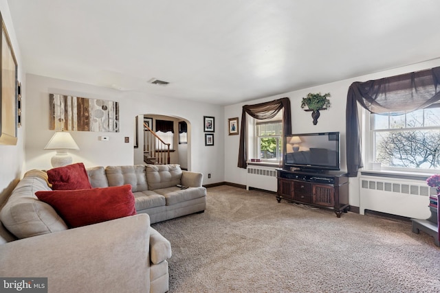 carpeted living area with arched walkways, visible vents, radiator, and stairs
