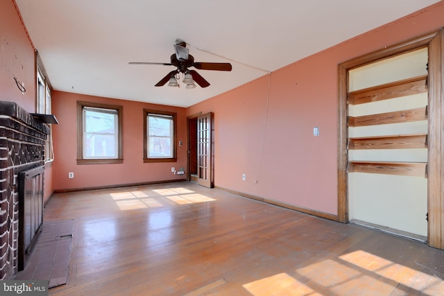 spare room with light wood-type flooring, a brick fireplace, ceiling fan, and baseboards