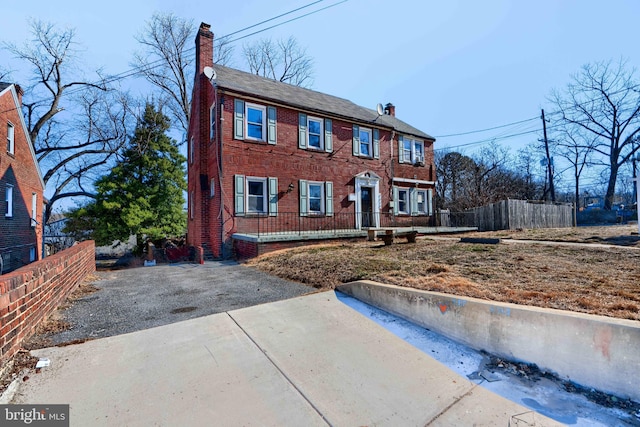 colonial house with a chimney, fence, and brick siding