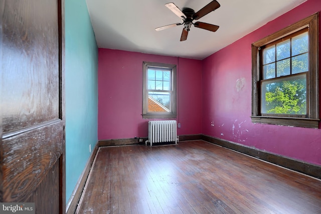 empty room with a ceiling fan, radiator heating unit, hardwood / wood-style flooring, and baseboards