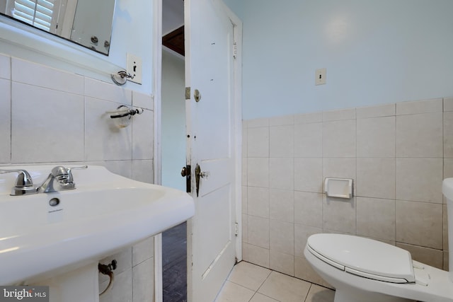 half bathroom featuring toilet, a sink, tile walls, and tile patterned floors