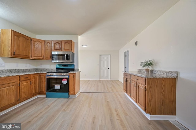 kitchen featuring light stone countertops, light wood-style floors, appliances with stainless steel finishes, and brown cabinetry