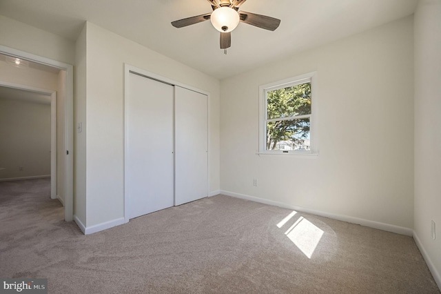 unfurnished bedroom featuring light carpet, a closet, a ceiling fan, and baseboards