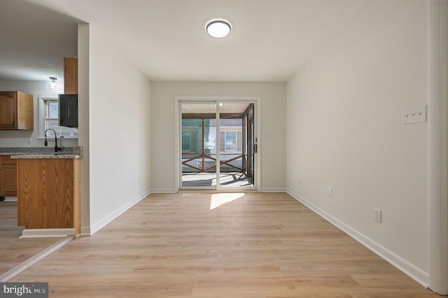 unfurnished dining area featuring light wood-type flooring, a sink, and baseboards