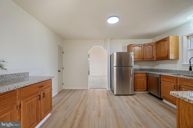 kitchen featuring stainless steel appliances, brown cabinetry, a sink, and light stone countertops