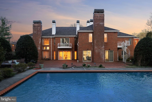 7707 Carlton Pl, Mclean, VA 22102 - back of house at dusk with an outdoor pool, stairs, a balcony, brick siding, and a chimney