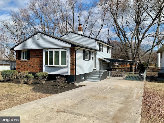 view of front of house featuring concrete driveway, brick siding, fence, and a chimney