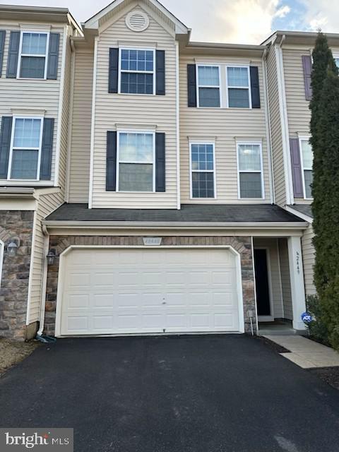 multi unit property featuring driveway, stone siding, and an attached garage