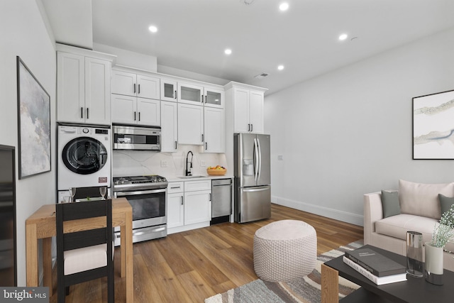 kitchen featuring stainless steel appliances, wood finished floors, a sink, white cabinetry, and backsplash