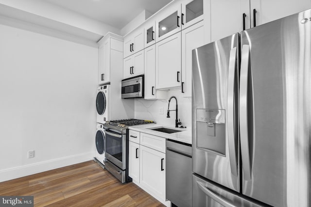 kitchen with dark wood finished floors, stainless steel appliances, tasteful backsplash, a sink, and stacked washing maching and dryer