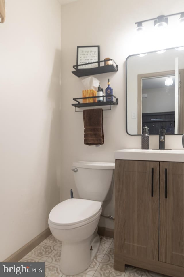 half bath with toilet, tile patterned floors, vanity, and baseboards