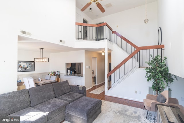 living area with ceiling fan with notable chandelier, visible vents, stairway, and wood finished floors