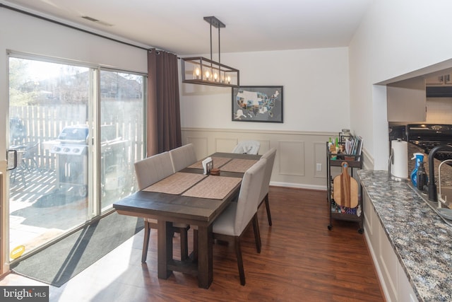 dining area with a notable chandelier, a wainscoted wall, a decorative wall, dark wood-style flooring, and visible vents