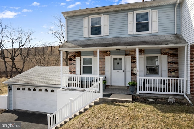 view of front of house featuring aphalt driveway, covered porch, brick siding, and roof with shingles