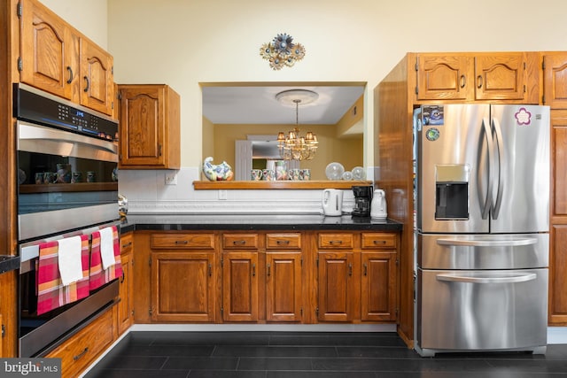 kitchen featuring stainless steel appliances, dark countertops, brown cabinets, and a notable chandelier