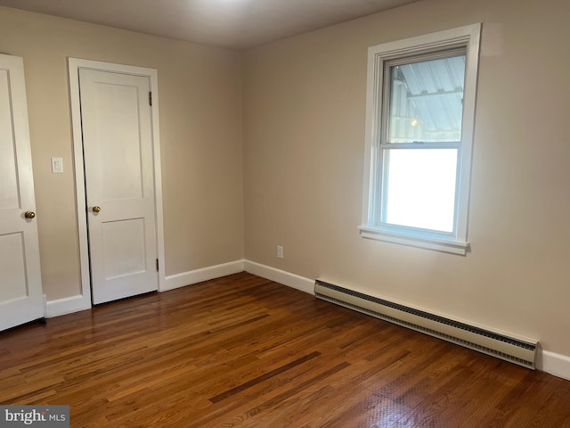 empty room featuring a baseboard heating unit, dark wood finished floors, and baseboards