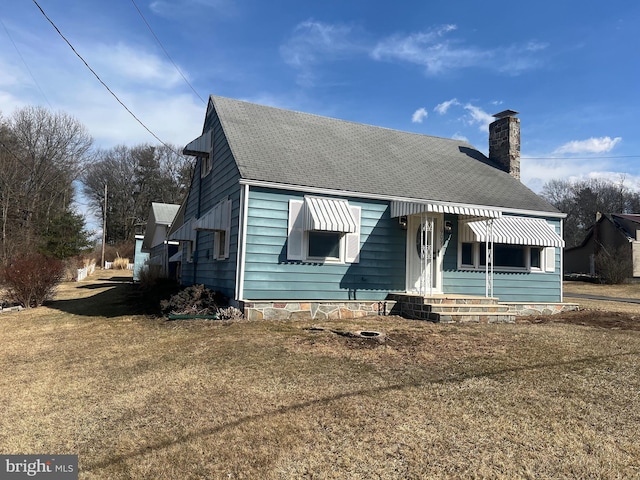 view of front facade featuring a chimney, a front yard, and a shingled roof