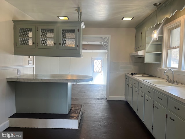 kitchen featuring decorative light fixtures, light countertops, glass insert cabinets, a sink, and under cabinet range hood