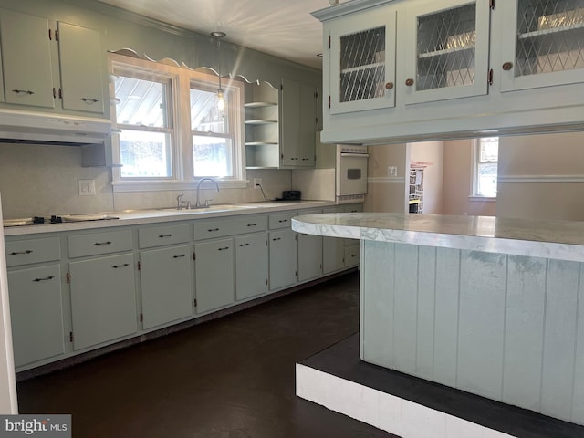 kitchen featuring under cabinet range hood, a sink, white cabinetry, light countertops, and pendant lighting