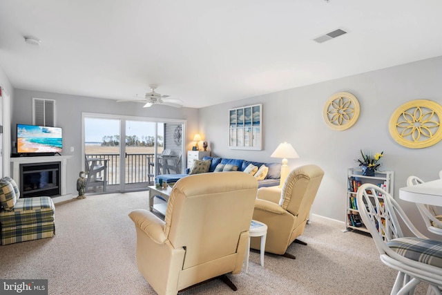 living area featuring visible vents, a ceiling fan, carpet, and a glass covered fireplace