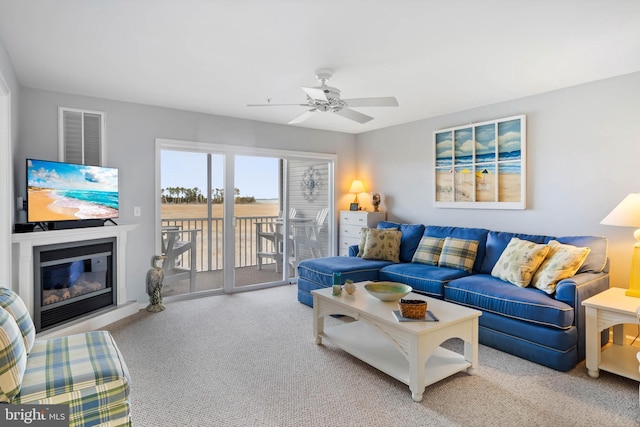 living area featuring ceiling fan, carpet, and a glass covered fireplace