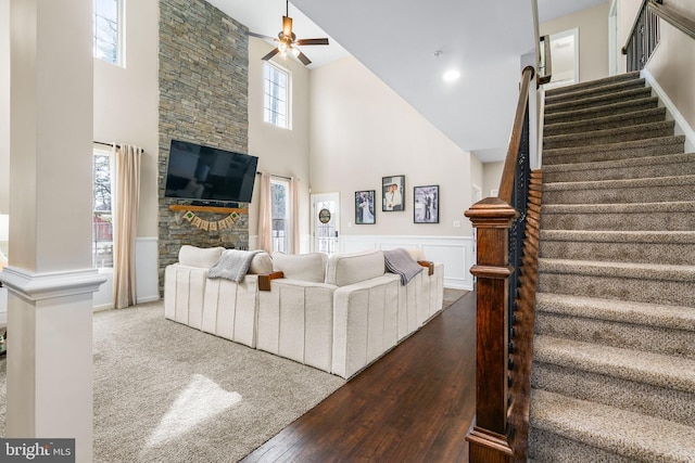 living area featuring a wainscoted wall, wood-type flooring, stairway, a high ceiling, and ceiling fan