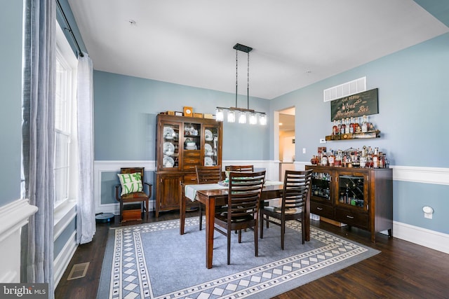 dining space featuring a wainscoted wall, visible vents, a dry bar, and wood finished floors