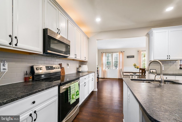 kitchen with white cabinets, dark wood finished floors, decorative backsplash, stainless steel appliances, and a sink