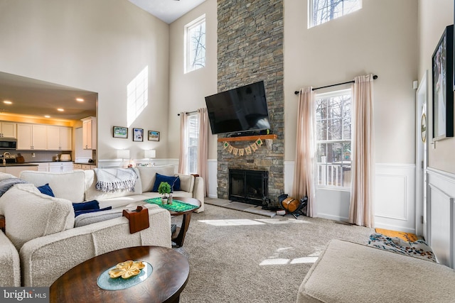 living area featuring a wainscoted wall, plenty of natural light, carpet flooring, and a stone fireplace