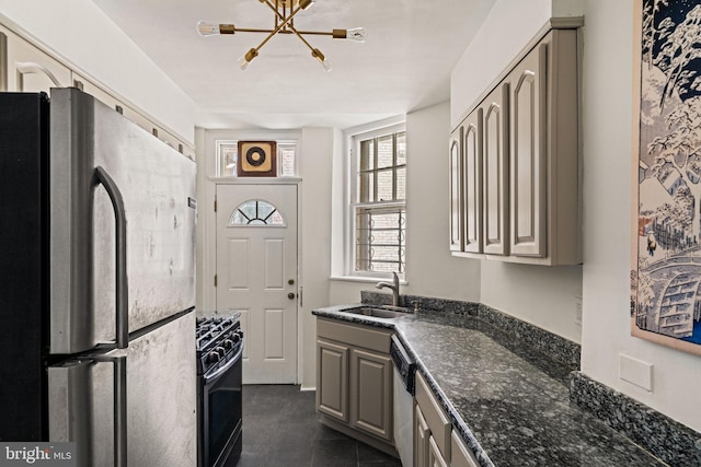 kitchen with appliances with stainless steel finishes, dark tile patterned flooring, a sink, and dark stone countertops