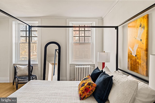 bedroom with ornamental molding, multiple windows, wood finished floors, and radiator